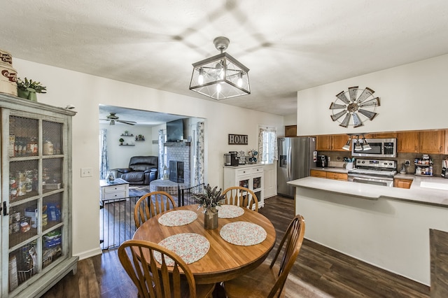 dining space with ceiling fan, a textured ceiling, dark hardwood / wood-style floors, and a fireplace