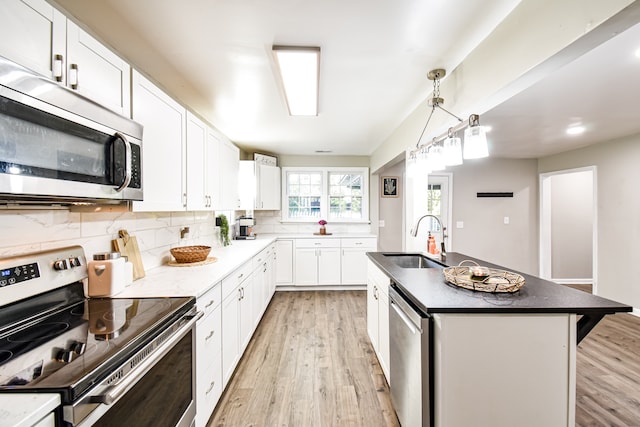 kitchen with sink, a kitchen island, white cabinetry, light wood-type flooring, and appliances with stainless steel finishes