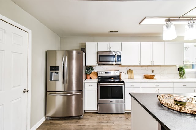 kitchen featuring white cabinetry, stainless steel appliances, light hardwood / wood-style floors, and backsplash