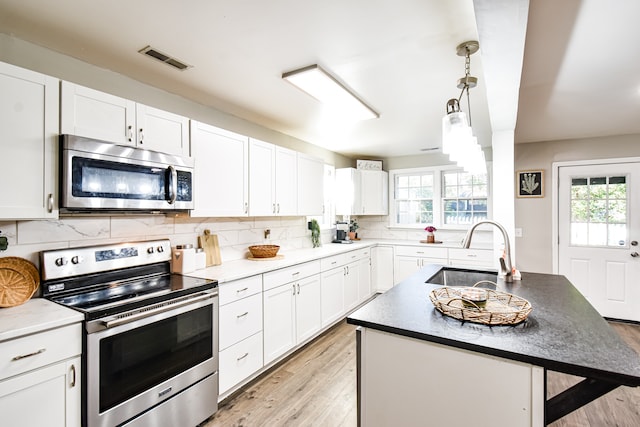 kitchen with light hardwood / wood-style flooring, a wealth of natural light, a kitchen island with sink, and stainless steel appliances