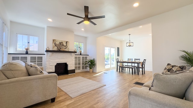 living room featuring a stone fireplace, light hardwood / wood-style floors, and ceiling fan