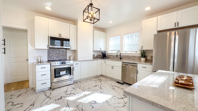 kitchen with white cabinetry, stainless steel appliances, hanging light fixtures, and light stone countertops