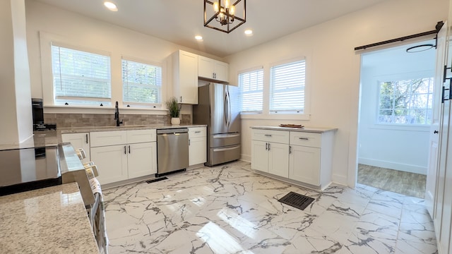 kitchen with appliances with stainless steel finishes, tasteful backsplash, decorative light fixtures, a chandelier, and white cabinets