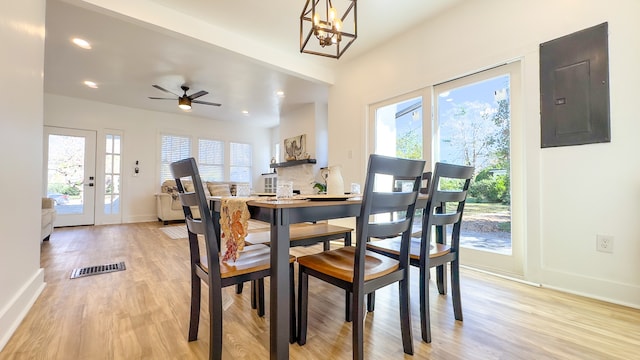 dining area with electric panel, light hardwood / wood-style floors, ceiling fan with notable chandelier, and a healthy amount of sunlight