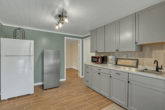 kitchen featuring sink, ornamental molding, gray cabinets, white fridge, and light hardwood / wood-style flooring