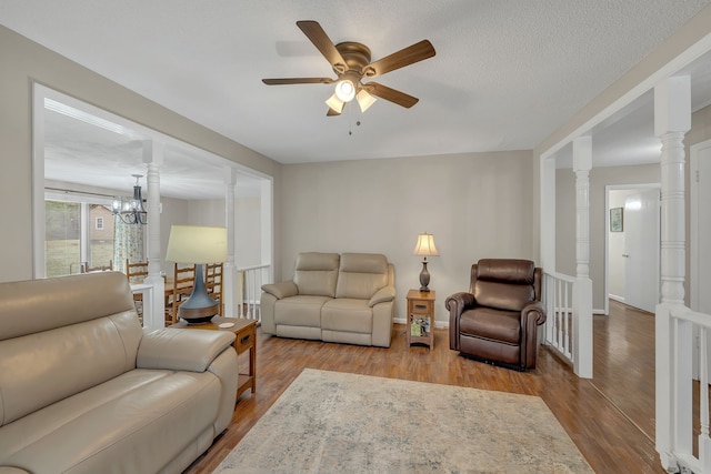 living room featuring light hardwood / wood-style floors, ceiling fan with notable chandelier, a textured ceiling, and ornate columns