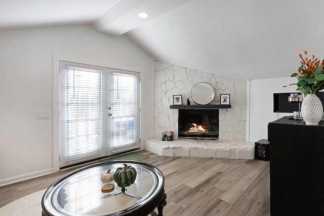 living room with a stone fireplace, lofted ceiling, and wood-type flooring