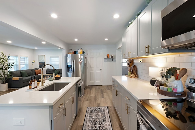 kitchen featuring tasteful backsplash, stainless steel appliances, sink, light hardwood / wood-style floors, and a kitchen island with sink