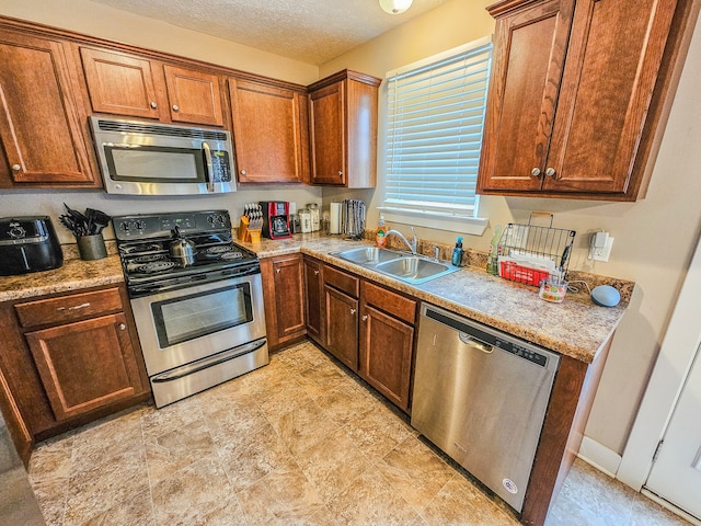 kitchen featuring light stone countertops, a textured ceiling, sink, and appliances with stainless steel finishes