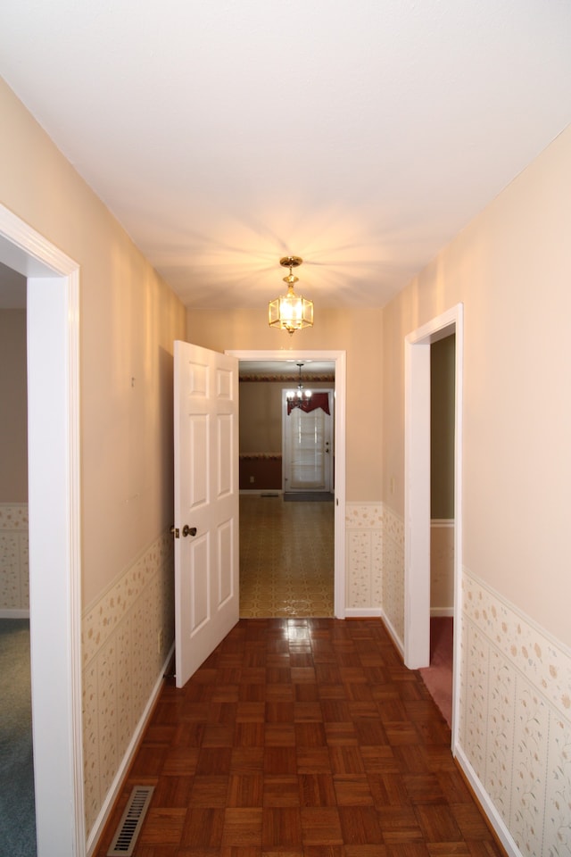 corridor featuring dark parquet flooring and a chandelier