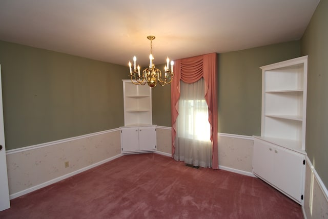 empty room featuring built in shelves, a chandelier, and carpet floors