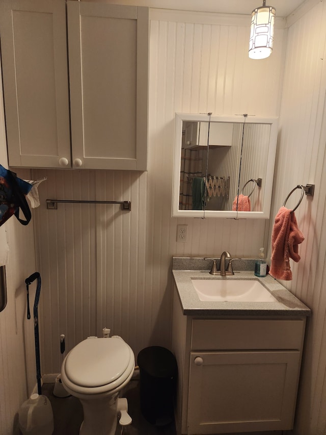 bathroom featuring wood walls, vanity, and toilet