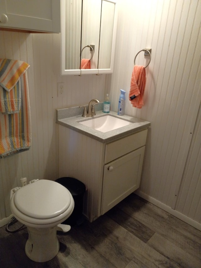 bathroom with wood-type flooring, vanity, toilet, and wood walls