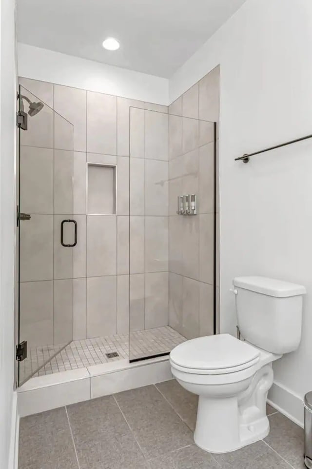 bathroom with tile patterned flooring, toilet, and a shower with shower door