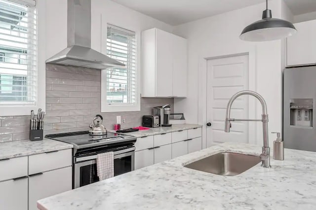 kitchen with white cabinets, stainless steel appliances, wall chimney exhaust hood, and light stone countertops