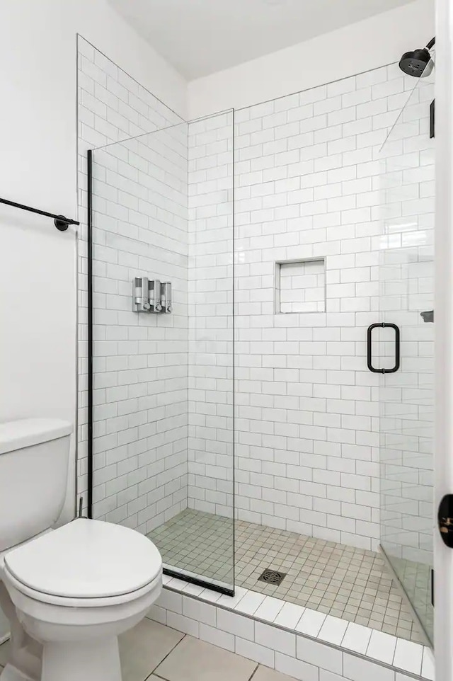 bathroom featuring toilet, tile patterned floors, and a shower with shower door