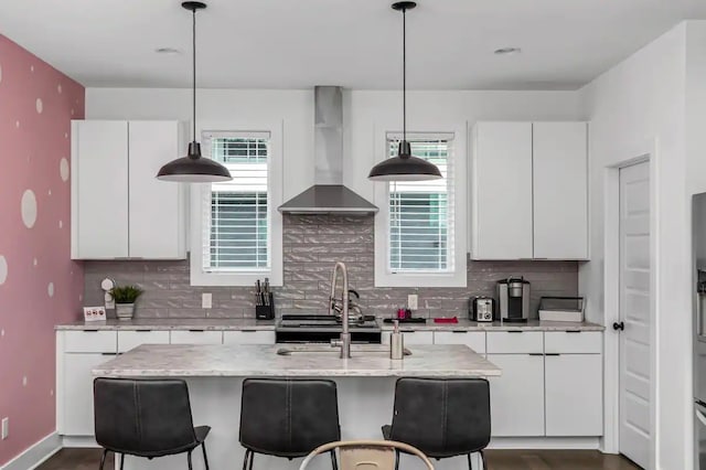 kitchen with white cabinetry, an island with sink, wall chimney range hood, and backsplash