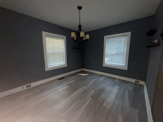 unfurnished dining area with wood-type flooring and an inviting chandelier