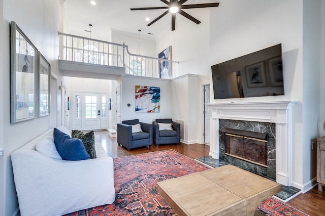 living room with dark hardwood / wood-style flooring, ceiling fan, a high end fireplace, and a high ceiling