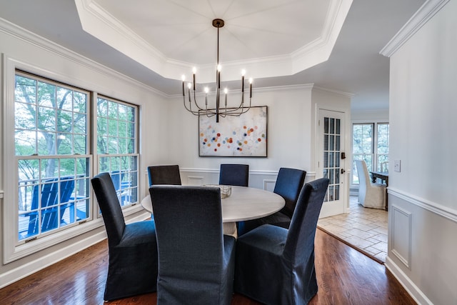 dining space featuring dark hardwood / wood-style floors, a notable chandelier, a raised ceiling, and ornamental molding