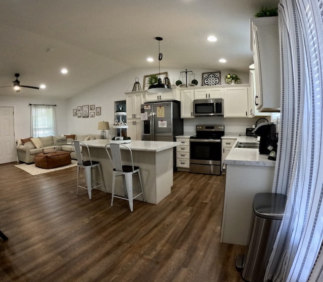 kitchen with stainless steel appliances, hanging light fixtures, a kitchen island, dark wood-type flooring, and vaulted ceiling