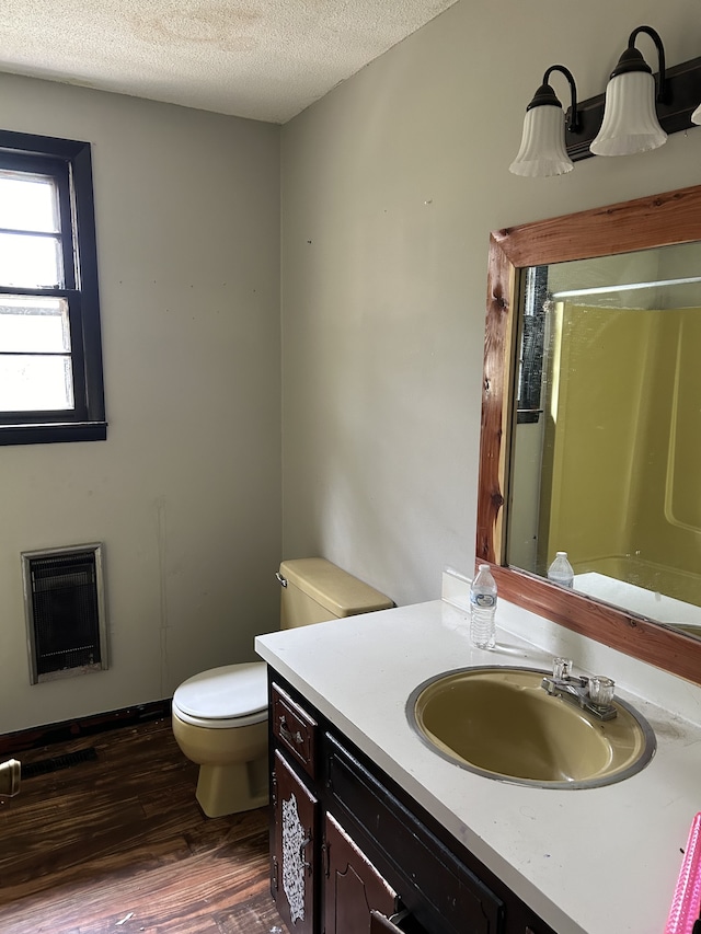 bathroom with heating unit, vanity, a textured ceiling, hardwood / wood-style flooring, and toilet