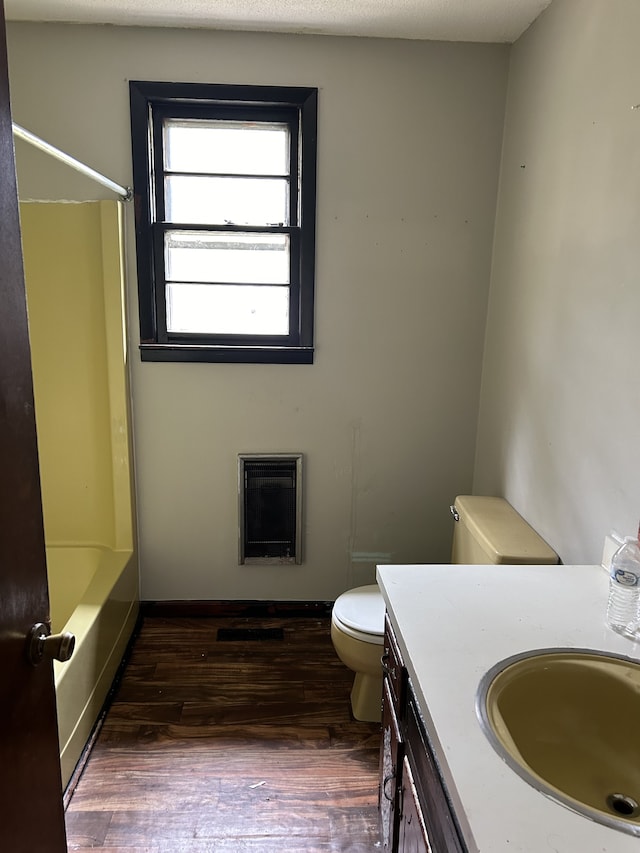 full bathroom featuring heating unit, vanity, a textured ceiling, hardwood / wood-style flooring, and toilet