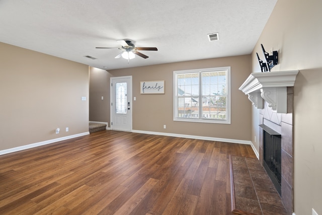 unfurnished living room with a tiled fireplace, ceiling fan, dark wood-type flooring, and a textured ceiling