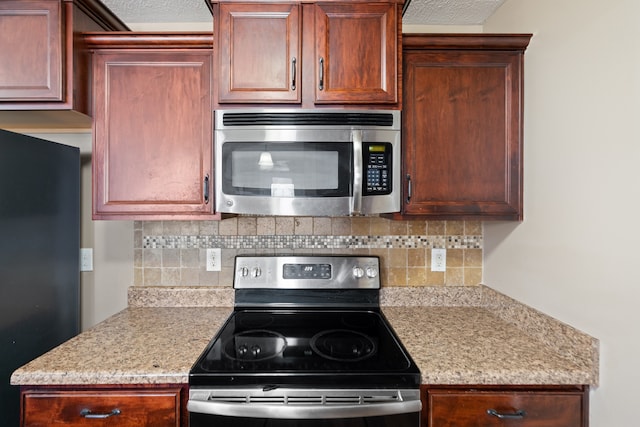 kitchen featuring decorative backsplash, light stone counters, a textured ceiling, and appliances with stainless steel finishes