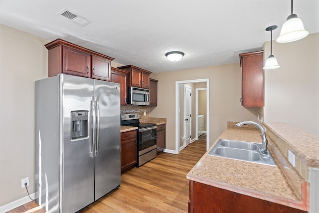 kitchen featuring appliances with stainless steel finishes, backsplash, sink, light hardwood / wood-style flooring, and hanging light fixtures