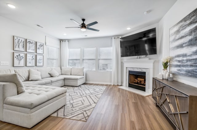 living room featuring light wood-type flooring, ceiling fan, and a high end fireplace