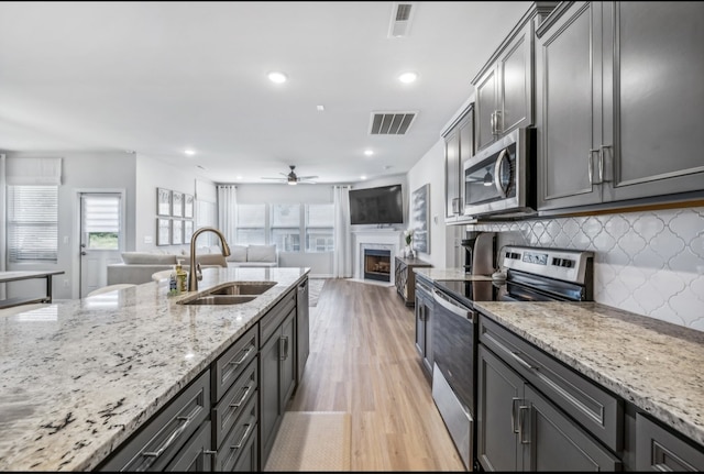 kitchen with light stone counters, light hardwood / wood-style flooring, sink, a fireplace, and appliances with stainless steel finishes