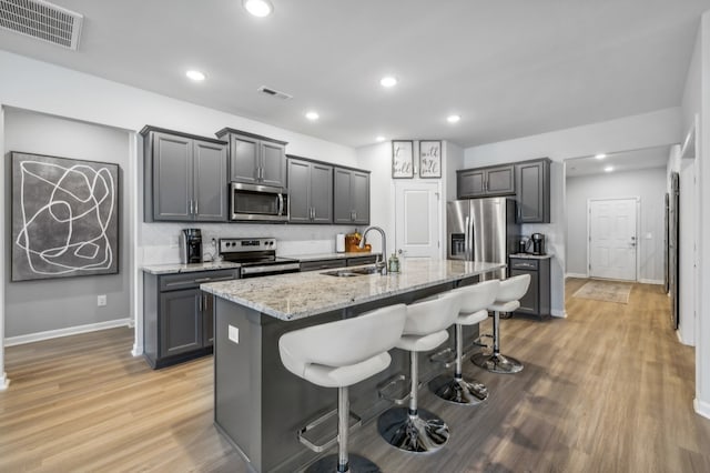 kitchen featuring wood-type flooring, a center island with sink, stainless steel appliances, sink, and a breakfast bar