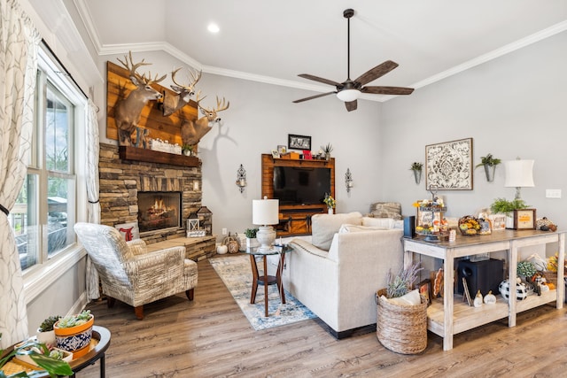 living room featuring ceiling fan, light hardwood / wood-style floors, a stone fireplace, and ornamental molding