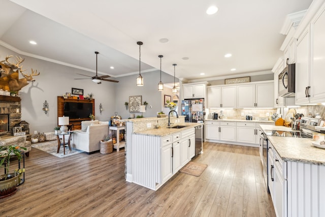 kitchen featuring a fireplace, appliances with stainless steel finishes, hanging light fixtures, white cabinets, and a kitchen island with sink