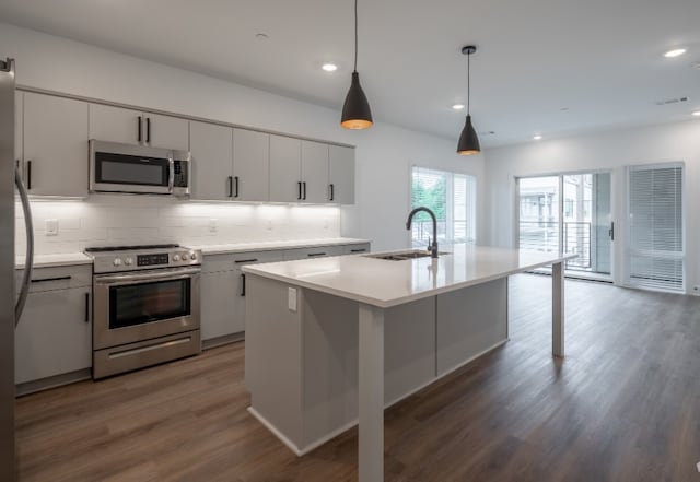 kitchen with dark wood-type flooring, sink, a kitchen island with sink, and appliances with stainless steel finishes