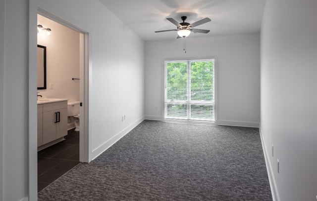 unfurnished room with ceiling fan, sink, and dark carpet