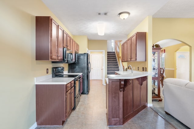 kitchen featuring kitchen peninsula, a textured ceiling, black electric range oven, and a breakfast bar