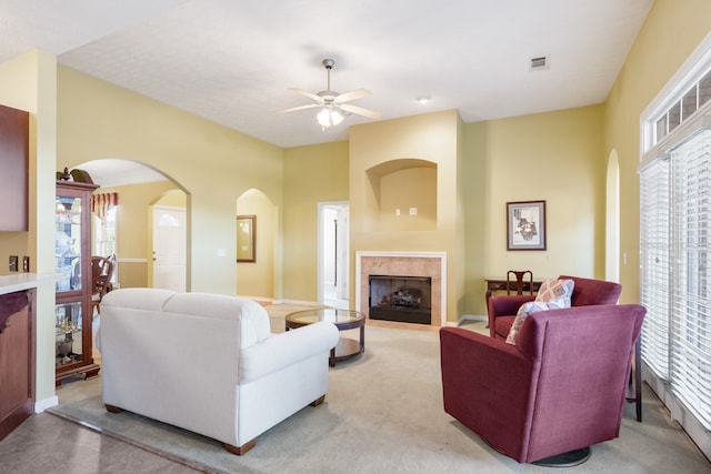 living room featuring a tiled fireplace, light carpet, and ceiling fan