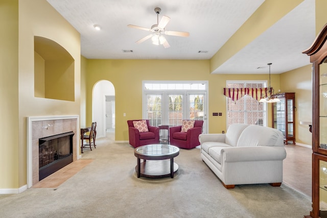 carpeted living room featuring ceiling fan with notable chandelier and a tiled fireplace