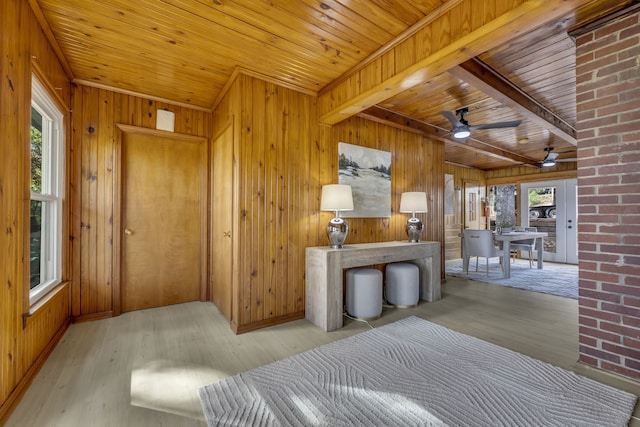 interior space featuring beam ceiling, light hardwood / wood-style floors, ceiling fan, and wooden walls