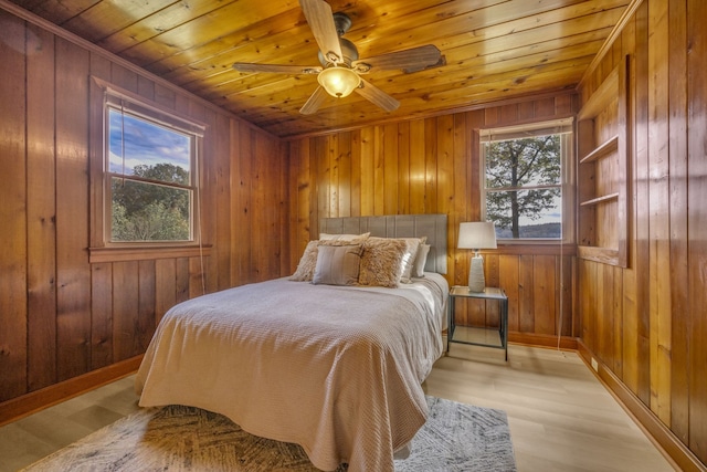 bedroom with light wood-type flooring, wooden ceiling, ceiling fan, and wooden walls