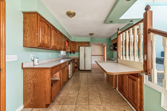 kitchen with white refrigerator, plenty of natural light, sink, light tile patterned floors, and dishwashing machine