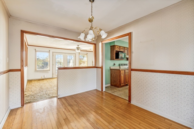 empty room with french doors, ceiling fan with notable chandelier, crown molding, and light hardwood / wood-style flooring