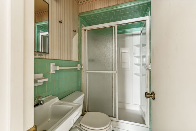 bathroom with toilet, an enclosed shower, tile walls, and sink