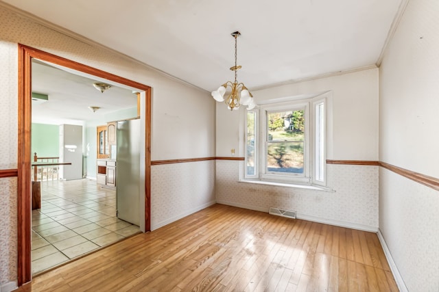 spare room featuring an inviting chandelier, light wood-type flooring, and ornamental molding