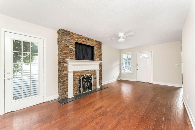 unfurnished living room with a textured ceiling, hardwood / wood-style flooring, a stone fireplace, and ceiling fan