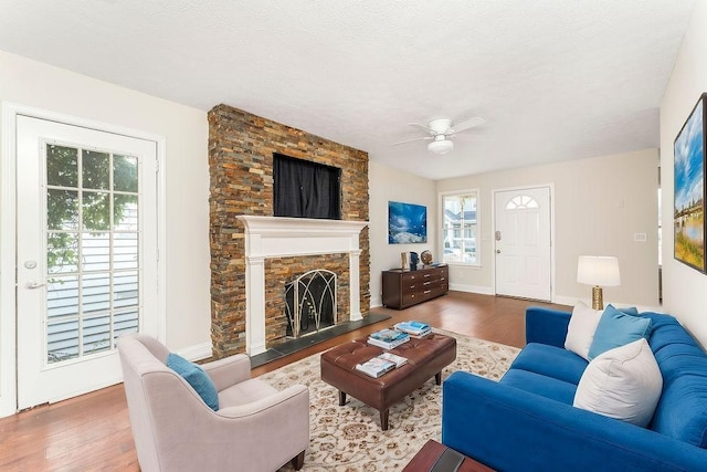 living room with hardwood / wood-style flooring, ceiling fan, and a stone fireplace