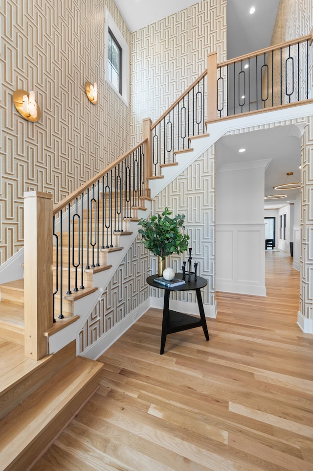 staircase featuring a towering ceiling, hardwood / wood-style flooring, and crown molding