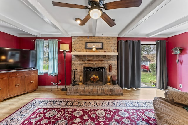 living room with ceiling fan, light hardwood / wood-style floors, beam ceiling, and a brick fireplace